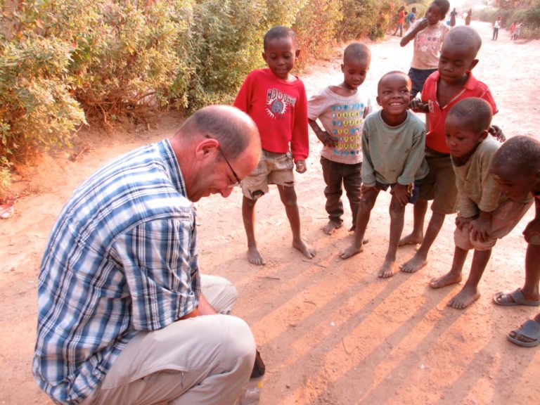 Gordon Binkhorst of Pure Earth crouches to use a hand-held XRF analyzer on the ground as a group of young children watch, in a neighborhood in Kabwe, Zambia.
